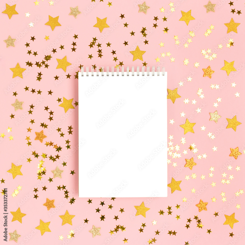 Notepad mockup on a pink pastel background with scattered gold stars confetti. Holidays concept.
