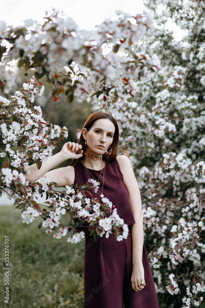 a beautiful brunette woman in a fashionable suit stands next to blooming Apple trees on a warm summer day. Stylish image for a walk in nature in the Park. a beautiful brunette woman in a fashionable suit stands next to blooming Apple trees on a warm summer day. Stylish image for a walk in nature in the Park.