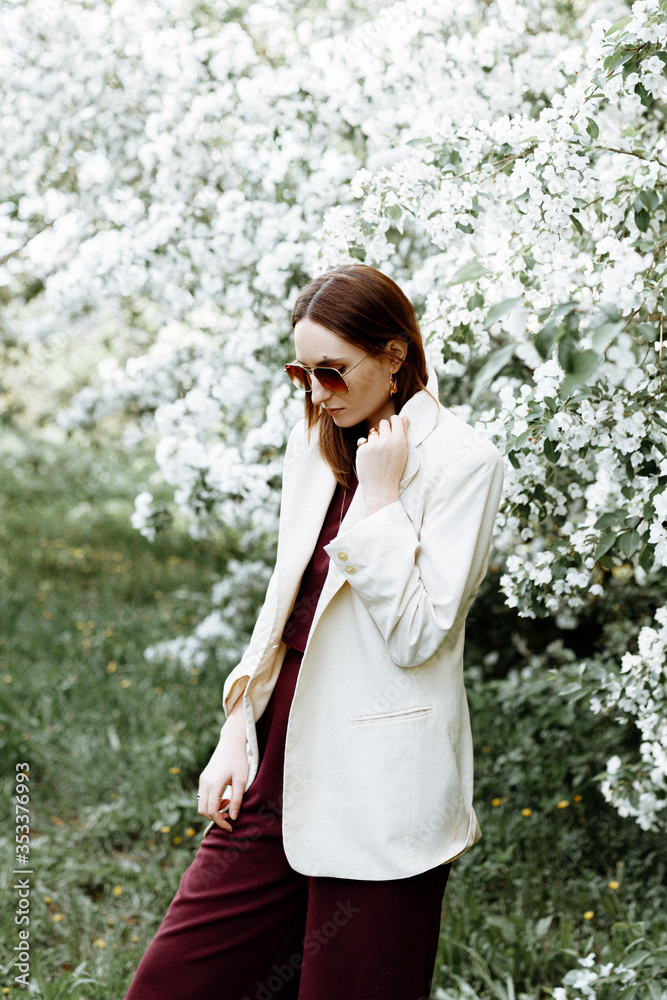 a beautiful brunette woman in a fashionable suit stands next to blooming Apple trees on a warm summer day. Stylish image for a walk in nature in the Park. a beautiful brunette woman in a fashionable suit stands next to blooming Apple trees on a warm summer day. Stylish image for a walk in nature in the Park.