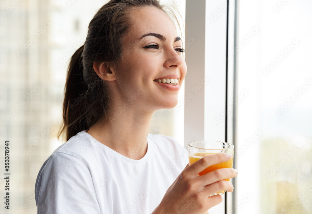 Image of pleased woman smiling and drinking fresh juice while standing Image of pleased woman smiling and drinking fresh juice while standing