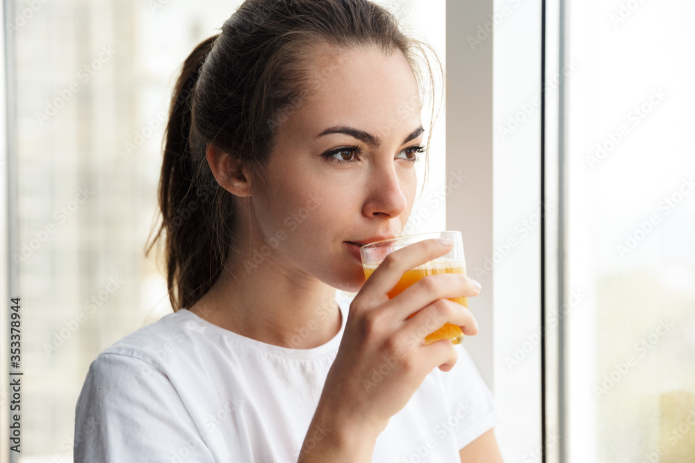 Image of focused woman drinking fresh juice while looking at window Image of focused woman drinking fresh juice while looking at window