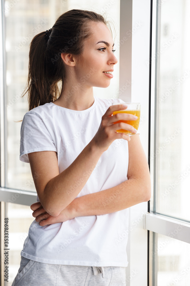 Image of pleased woman smiling and drinking fresh juice while standing Image of pleased woman smiling and drinking fresh juice while standing