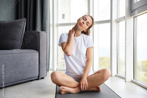 Image of focused young woman stretching her neck while sitting on yoga