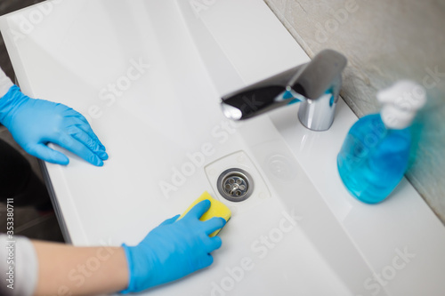 Woman hands in blue protective gloves using sponge to clean basin sink in bathroom. © zphoto83