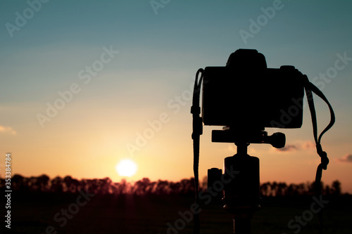 silhouette of a camera on a tripod that shoots a red sunset on the lawn