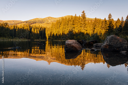 Beautiful landscape with mountains illuminated, reflection in mountain lake, blue sky and yellow sunlight. Slovakia, Vrbicke Pleso photo
