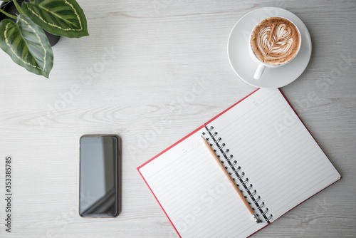 Top view of Notebook with pencil , Smart phone and cup of coffee on white wooden table.