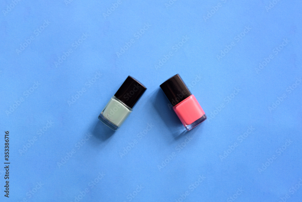 Fototapeta premium Two bottles with pink and mint color nail polish on a blue background. Top view, copy space. Manicure art cosmetic concept. Nail art