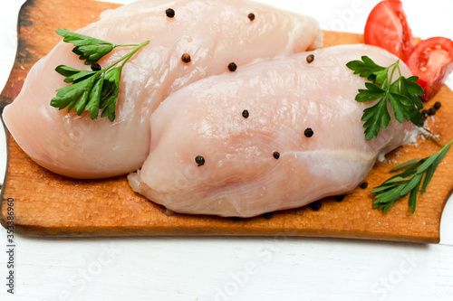 Raw chicken breast fillets on wooden cutting board with herbs and spices. 