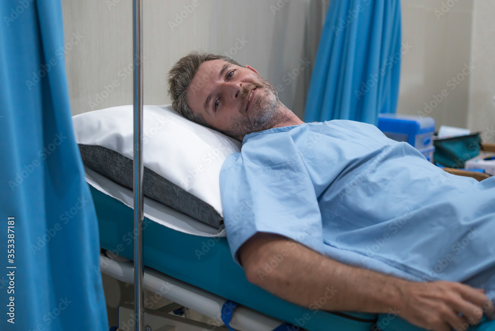 Obraz premium positive and hopeful hospital patient smiling before adversity - young attractive and trustful man lying on clinic bed responding to treatment and healing feeling relaxed