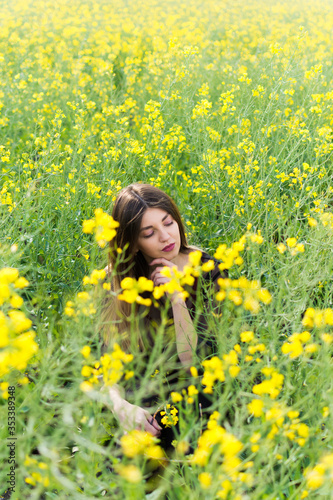 Girl in dark clothes with beautiful hair sitting in a field of yellow rape. Warm spring day