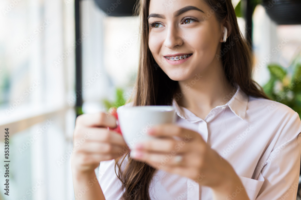 Smiling young woman at the cafe with headphones listening to music or talking on the phone