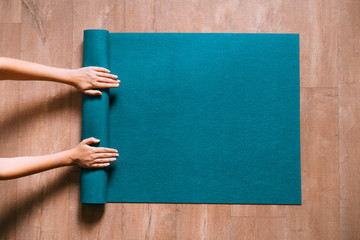 Fototapete Yogaschule Fit woman folding blue exercise mat on wooden floor before or after working out in yoga studio or at home. Equipment for fitness, pilates or yoga, well being concept. Flat lay, space for text.  © Anastasia Gubinskaya