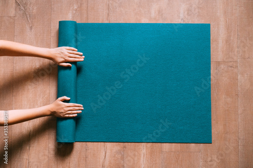Fit woman folding blue exercise mat on wooden floor before or after working out in yoga studio or at home. Equipment for fitness, pilates or yoga, well being concept. Flat lay, space for text.