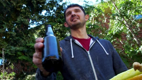 High quality close-up 4k video of a young blurred man on a bright summer nature background having fun and snacks with bottle of beer. Happy outdoor summer time. Handsome person smiling and laughing.