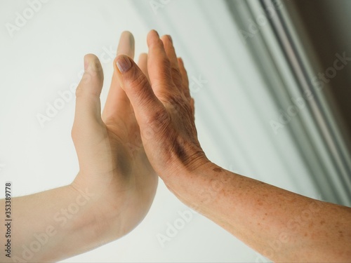 Close up of hands of elderly and young women on window photo