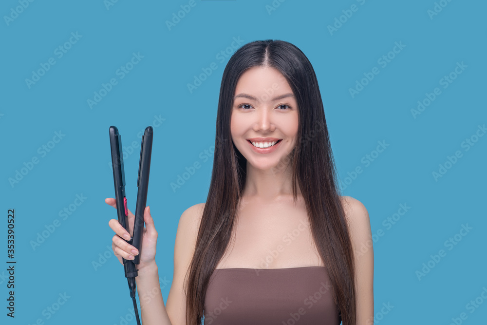 Young asian woman holding hair straightening iron and smiling nicely Young asian woman holding hair straightening iron and smiling nicely