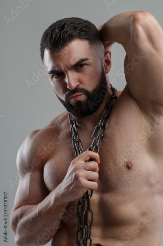 Portrait athletic handsome man with a beard with a chain Isolated on a gray background.