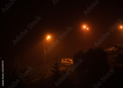 Night city ghetto, view from the window on parking lot with cars and high yellow, orange street lights in dangerous residential district in Ukraine with a copy space 