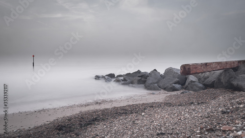 Long exposure of waves over rocks with washed up wooden plank and red warning marker