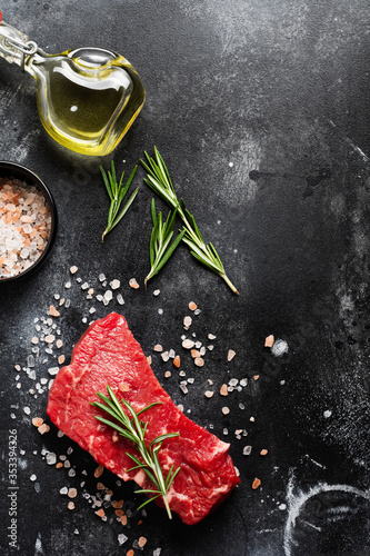 Raw beef steak with spices, onions and rosemary on dark slate or concrete background. Top view