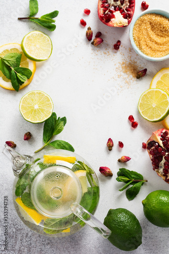 Fresh lemon  lime  pomegranate  dried tea rose flowers  tea  cane sugar  mint leaves and glass teapot on gray background. Ingredients for making cold refreshing fruit tea. Top view.