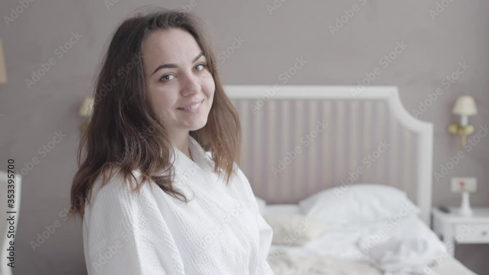 Young brunette woman turning to camera and smiling. Portrait of positive happy Caucasian girl posing in hotel room in the morning. Leisure, joy, lifestyle, happiness, tourism. Young brunette woman turning to camera and smiling. Portrait of positive happy Caucasian girl posing in hotel room in the morning. Leisure, joy, lifestyle, happiness, tourism.