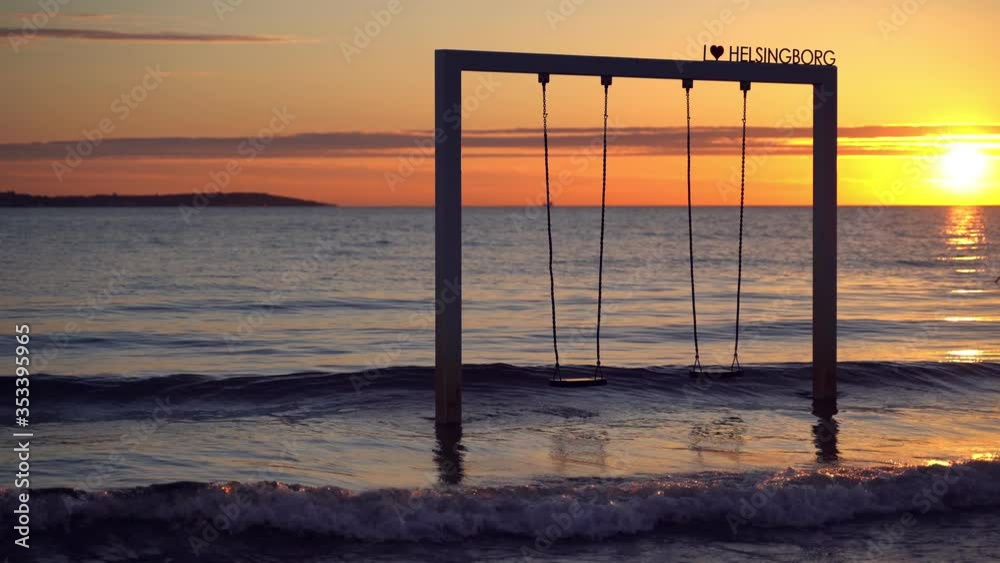 Empty swing in sea moving at sunset on the beach with the sun in the background, Helsingborg, Sweden Empty swing in sea moving at sunset on the beach with the sun in the background, Helsingborg, Sweden