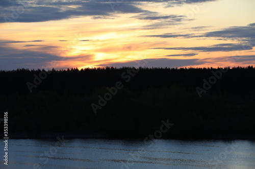 Fantastic panorama of the burning sky at dawn over the silhouette of the forest tops.Orange space with black streaks of clouds.Contrast of the bright flaming horizon with the darkness of night