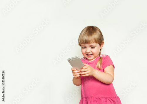 Cute beautiful blonde little girl playing with phone and malking photos and selfie on camera 