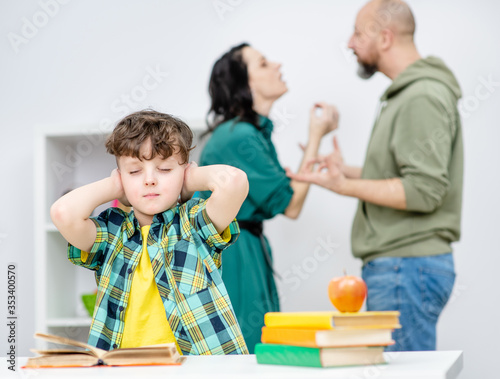 Unhappy boy covers his ears with hands and closes his eyes during parents quarrel photo