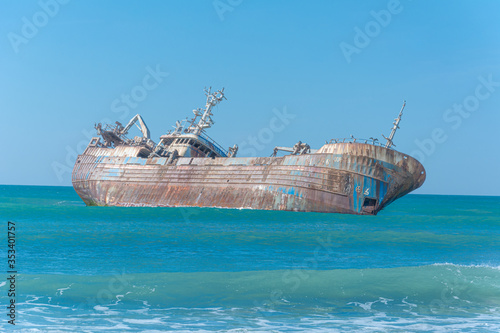 Fototapeta Naklejka Na Ścianę i Meble -  Laayoune port, Morocco, Western Sahara - January 6, 2019: a rusty shipwreck lies on its side under the blue sky in the Atlantic Ocean. Copy space
