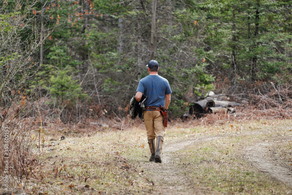 Man walking in the woods wearing handgun.