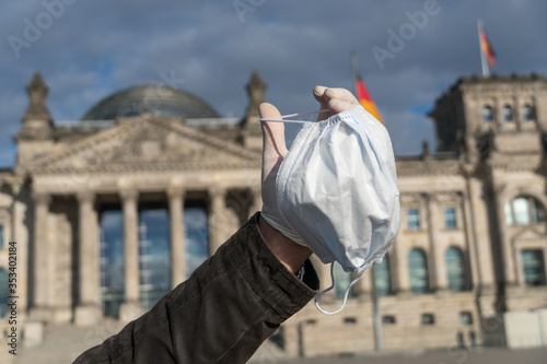 Using surgical masks outdoors. Man's hand covered by latex glove showing a medical protective mask outside the German Bundestag in Berlin, Germany. Selective focus