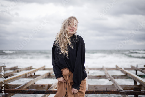 Beautiful young girl on a background of the sea. Blonde portrait photo. Autumn, cloudy weather, the sea is raging 