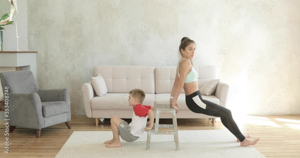 Mom and son training together doing exercise for triceps at home, side view. Sporty fit family doing fitness aerobic exercises for hands in living room. Home workout, training and wellness concept. Mom and son training together doing exercise for triceps at home, side view. Sporty fit family doing fitness aerobic exercises for hands in living room. Home workout, training and wellness concept.