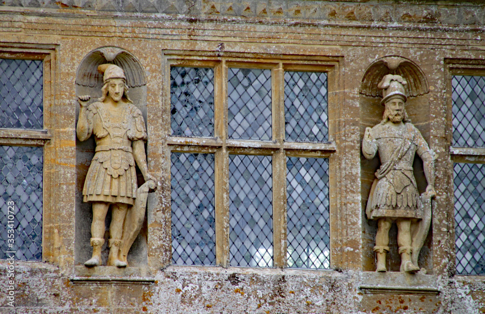 Two carved figures stand either side of leaded windows at an English country house in Somerset