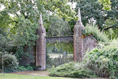 Old wrought iron gates mounted between two tall slim brick gate posts in an English country garden. photo