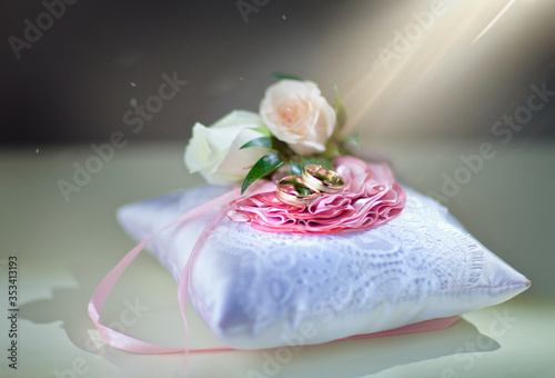 Wedding rings lie on a white pillow with ribbons and roses