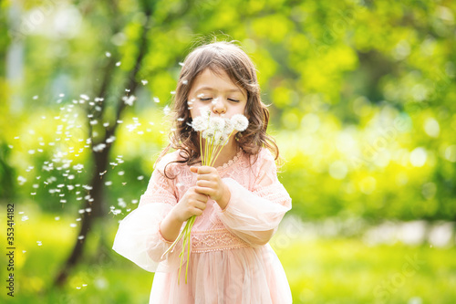 Little girl child cute and beautiful with a bunch of dandelions blowing on them in nature