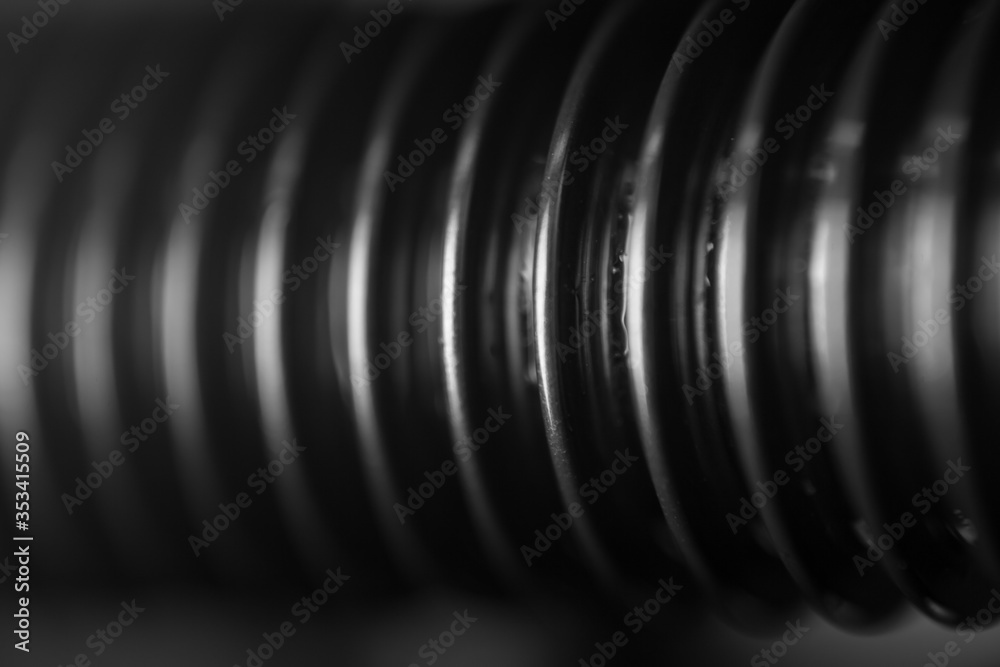 A close-up of the thread of a black bolt with whitening ribs of a spare part in an auto service as a background for publication in a thematic men's magazine.