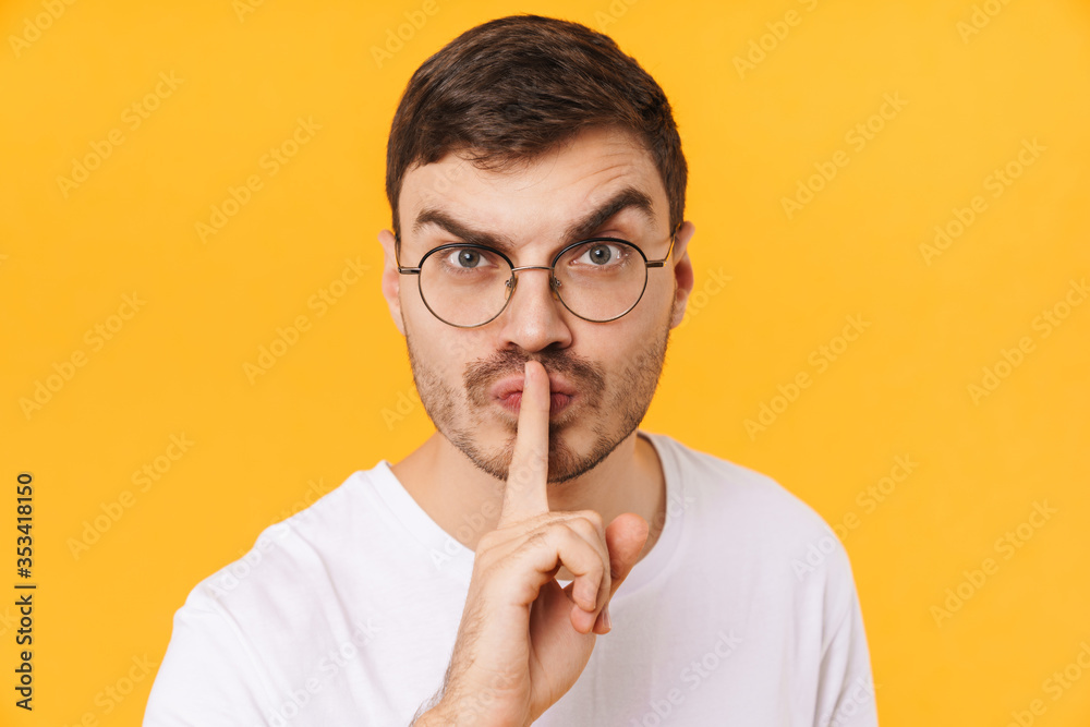Photo of displeased young man in eyeglasses showing silence gesture Photo of displeased young man in eyeglasses showing silence gesture