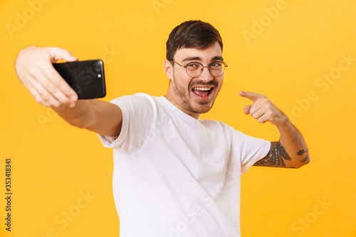 Photo of joyful young man taking selfie and pointing fingers