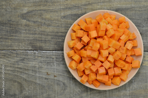 cuts cubes of carrot in white plate on wooden background