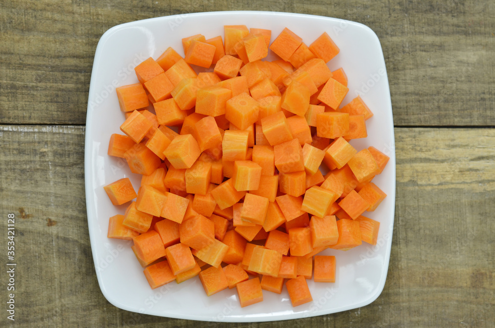 cuts cubes of carrot in white plate on wooden background cuts cubes of carrot in white plate on wooden background