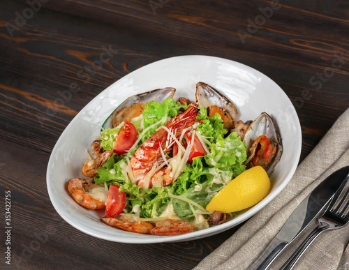 Seafood, tomato and lettuce salad sprinkled with grated parmesan on a background of dark boards