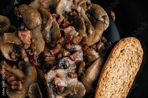 Cooked mushrroms with ham pieces on a black plate photo