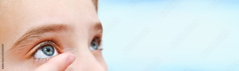 Little girl child putting contact lens into her eye isolated on a blue background - obrazy, fototapety, plakaty 