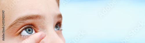 Little girl child putting contact lens into her eye isolated on a blue background