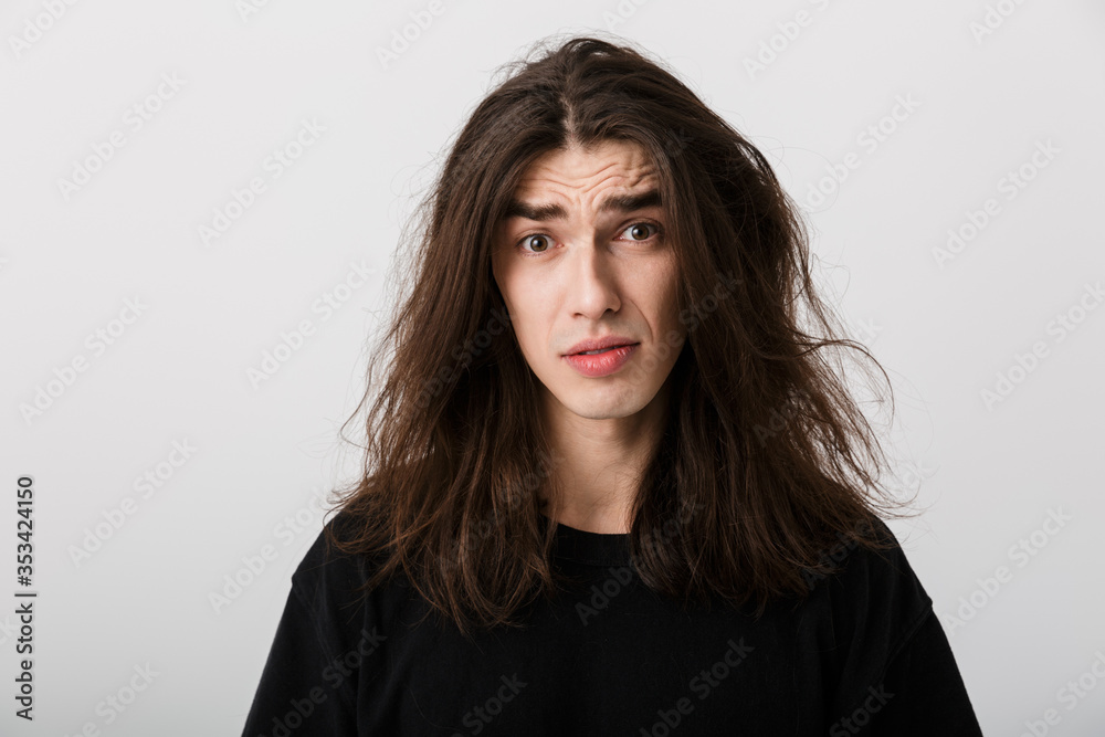 Portrait of handsome confused man with long hair poising and looking at camera